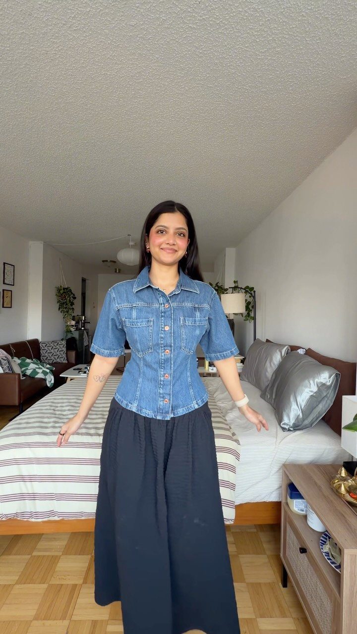 Woman posing in a blue denim shirt and a long black skirt indoors.