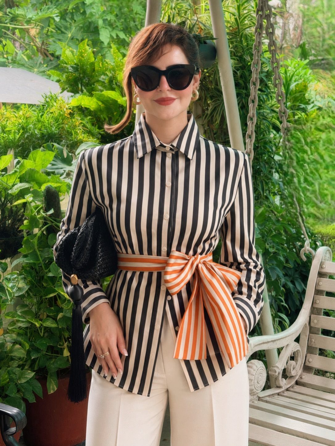 Woman in a black and white striped shirt with an orange bow belt and white trousers.