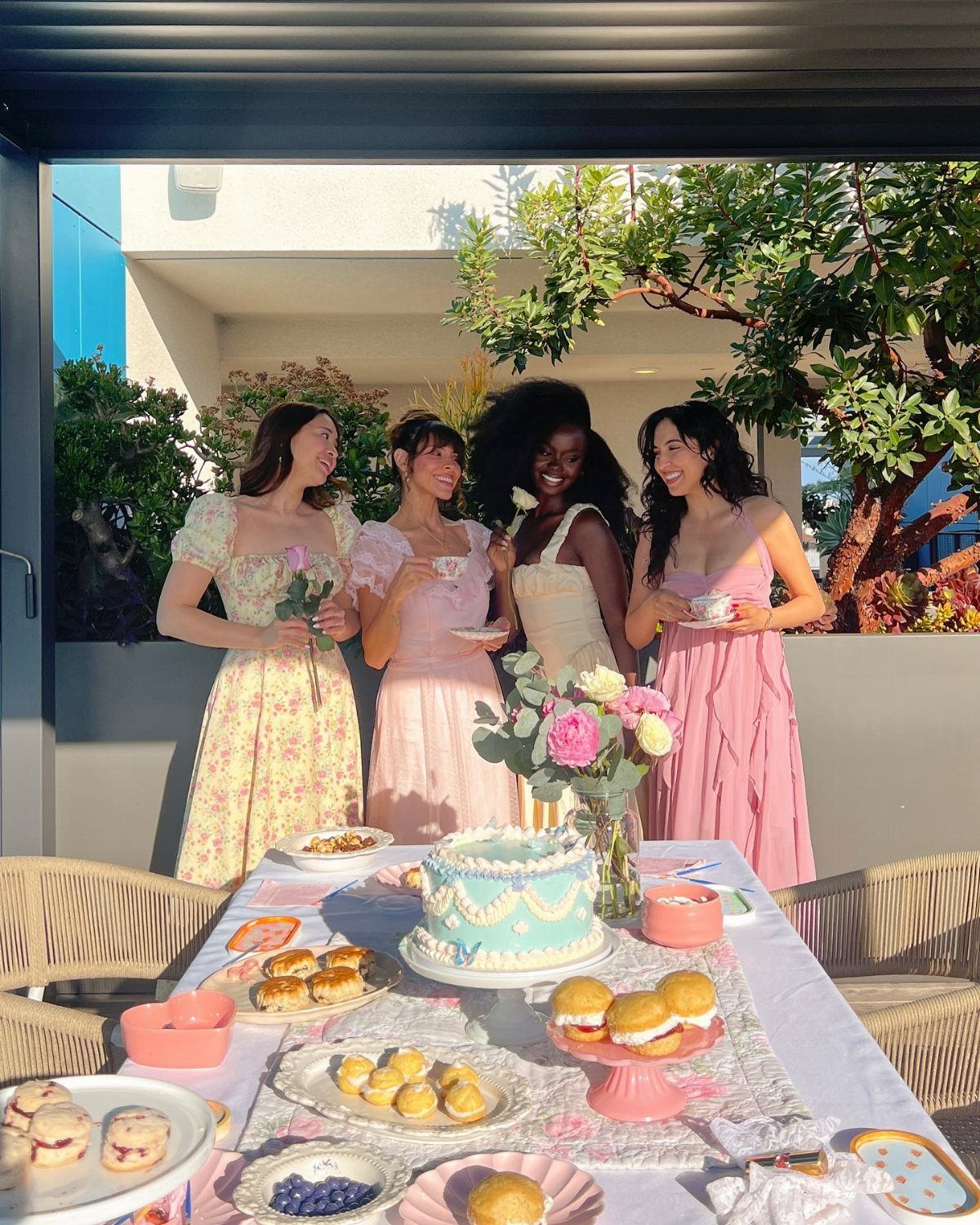 Tea Party Dresses: 6 Outfit Ideas for Brunches and Garden Events 2 Four women in pastel dresses standing behind a table filled with tea party treats and flowers.