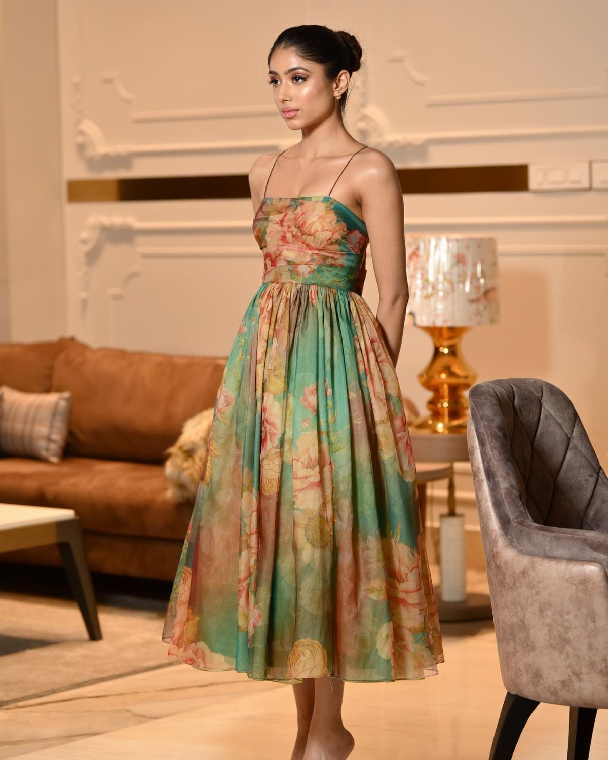 12 Tea Party Outfit Ideas for Women: Dresses, Hats & Accessories 5 A woman posing in a teal and peach floral midi dress within a living room.