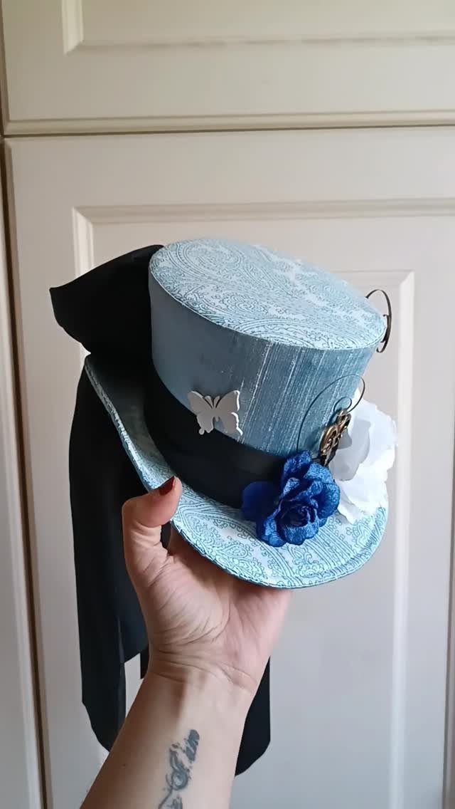 12 Tea Party Outfit Ideas for Women: Dresses, Hats & Accessories 9 A hand holding a light blue mini top hat decorated with blue and white flowers and a butterfly.