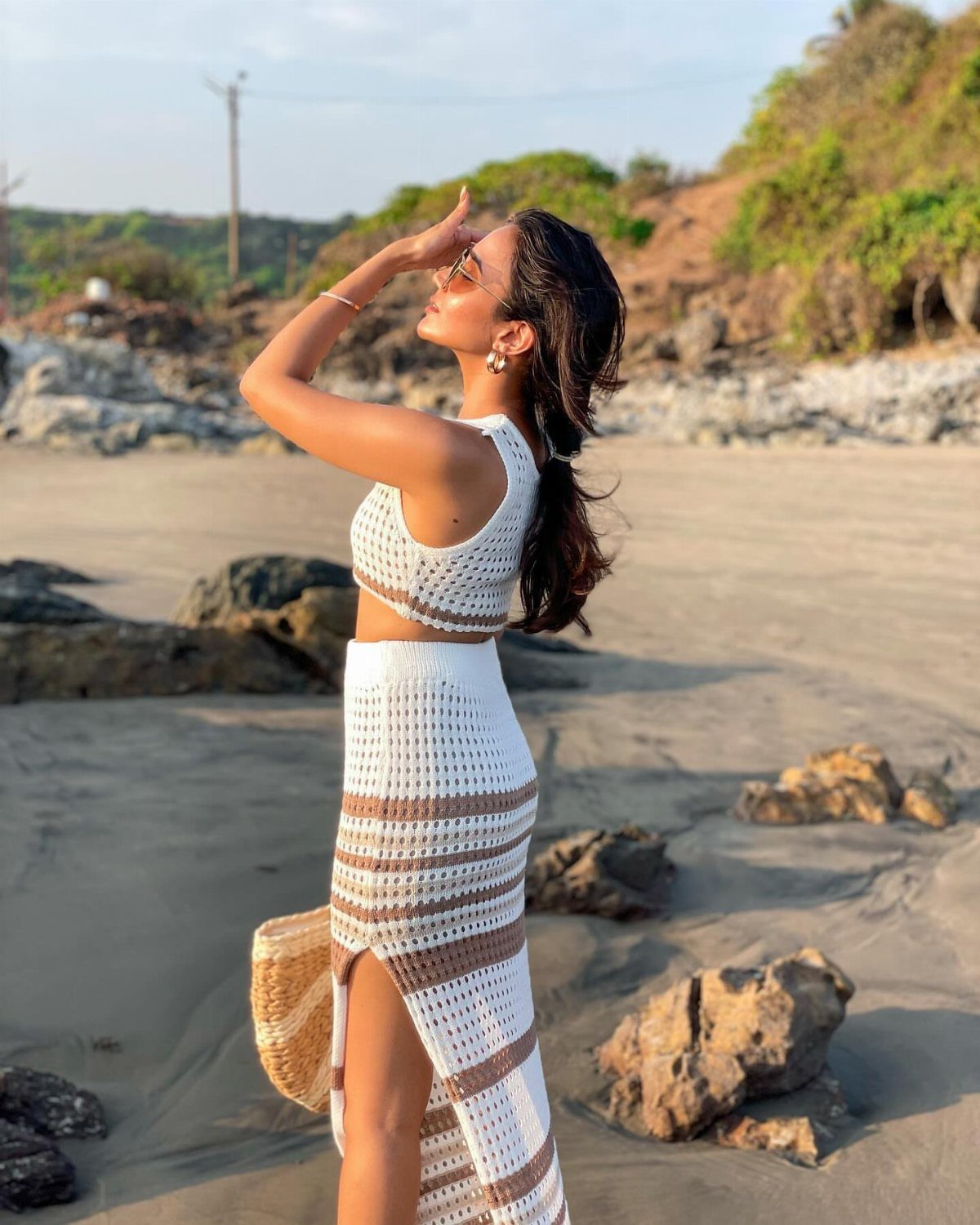 Woman in a white crochet crop top and long skirt posing on a sandy beach.