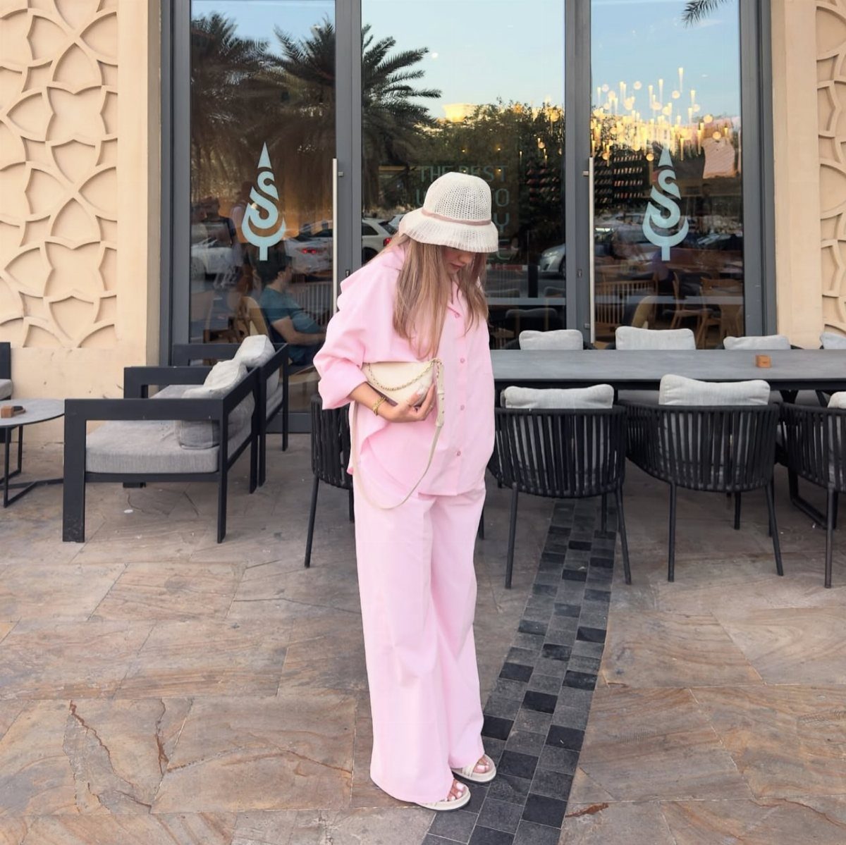 Woman wearing a light pink linen co-ord set and a white bucket hat standing outdoors.
