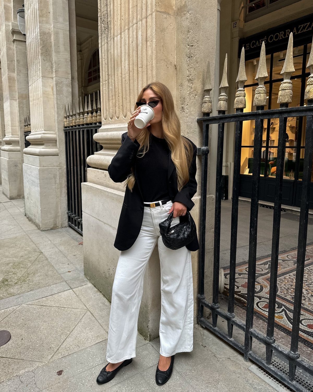 Woman wearing a black blazer and wide-leg white jeans standing on a city street.