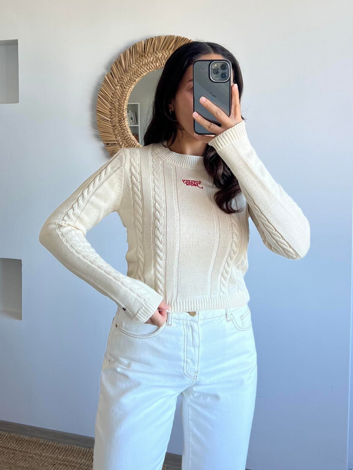 Woman wearing a cream cable-knit sweater and white wide-leg jeans in a mirror selfie.