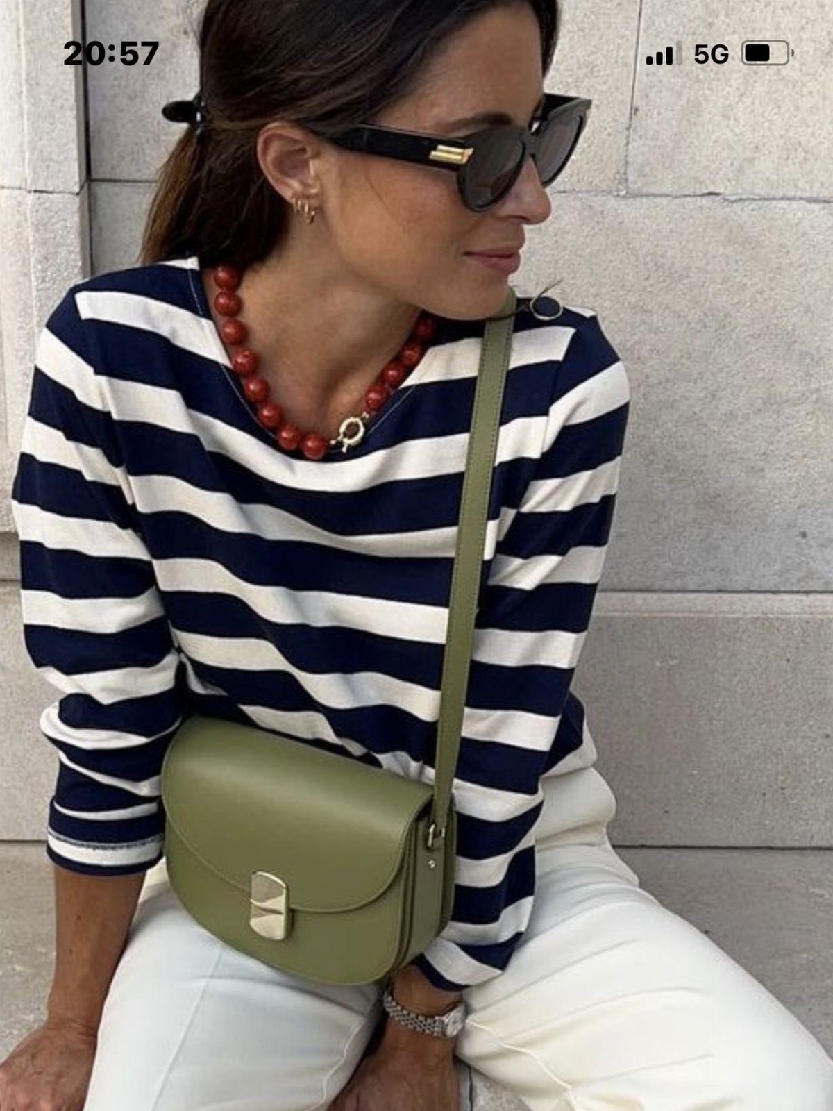 Woman wearing a navy Breton striped top and white pants with an olive bag.