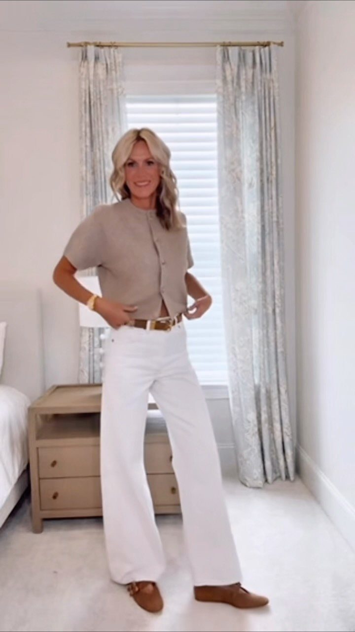 Woman wearing a beige top, wide-leg white jeans, and brown loafers in a bedroom.