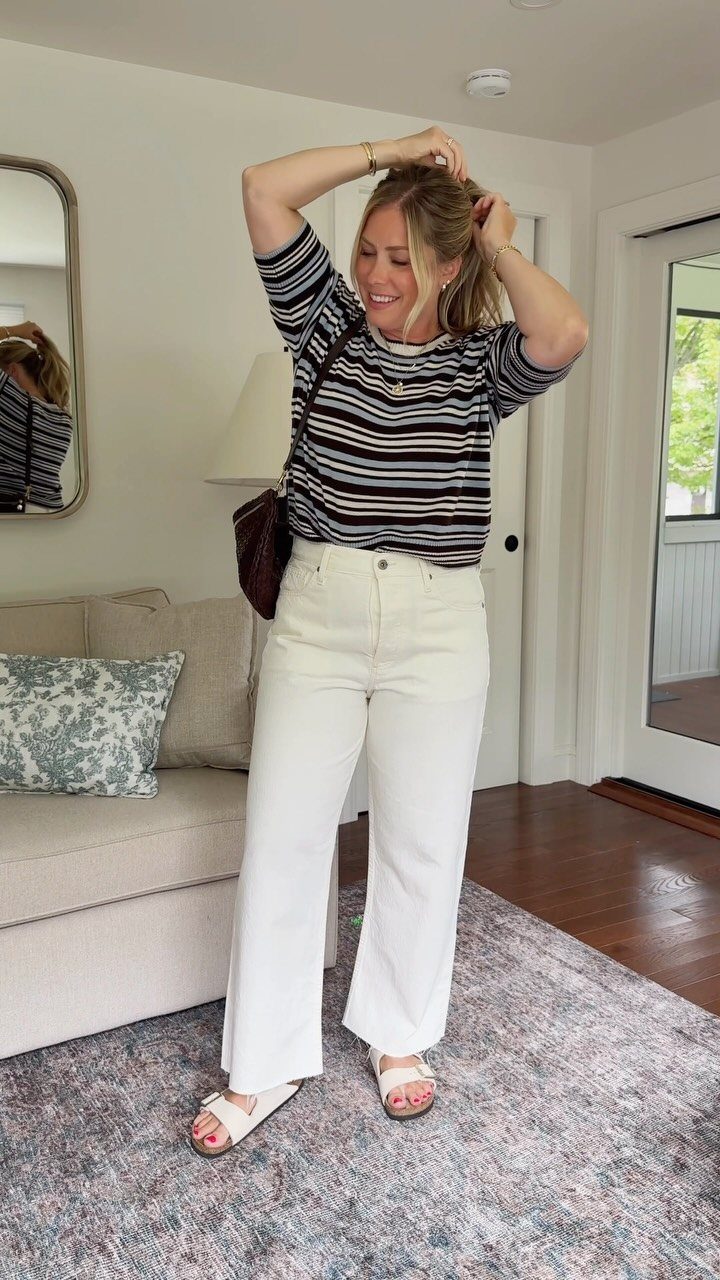 Woman wearing a striped top and wide-leg white jeans in a living room.