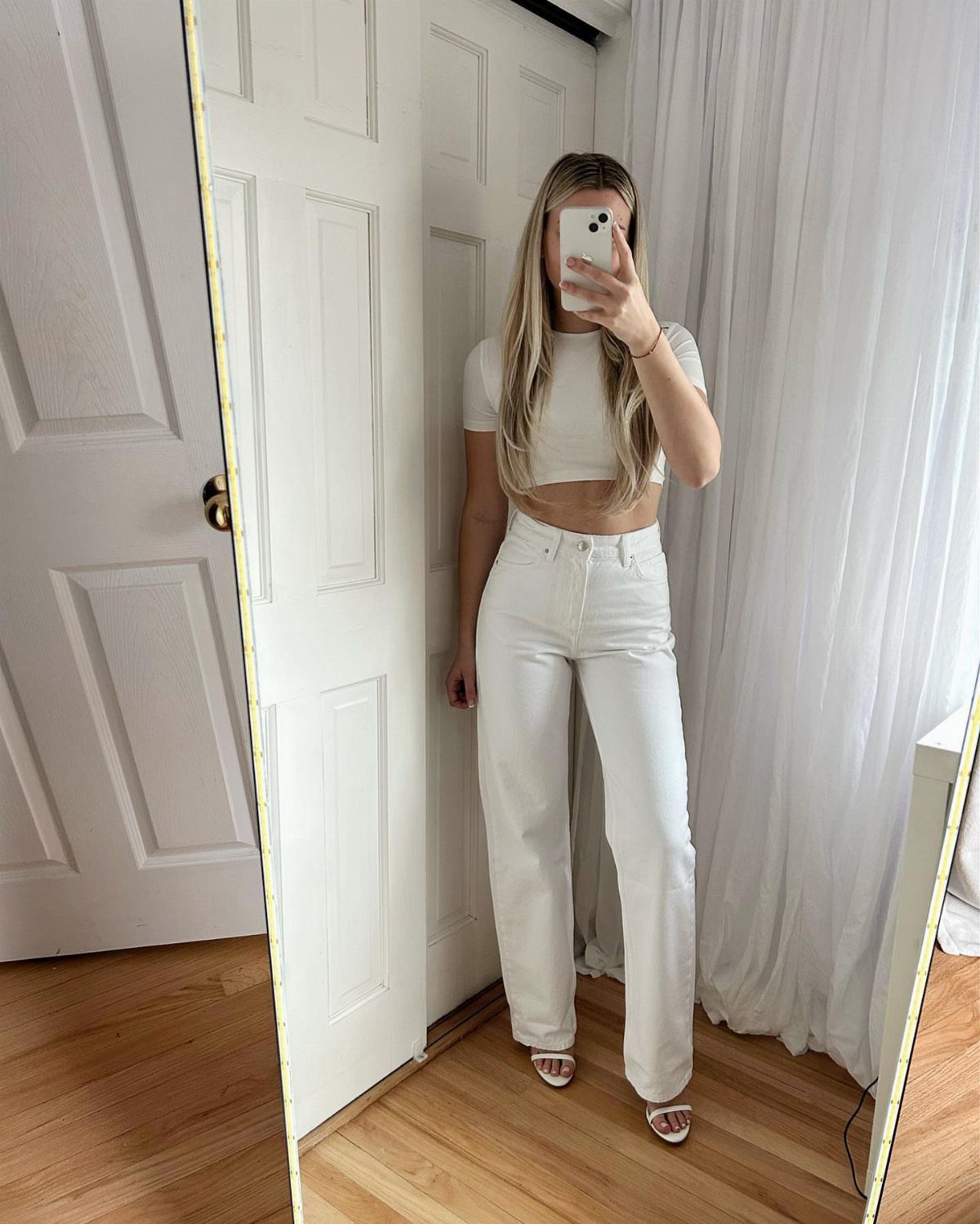 Woman in white crop top and white wide-leg jeans taking a mirror selfie.