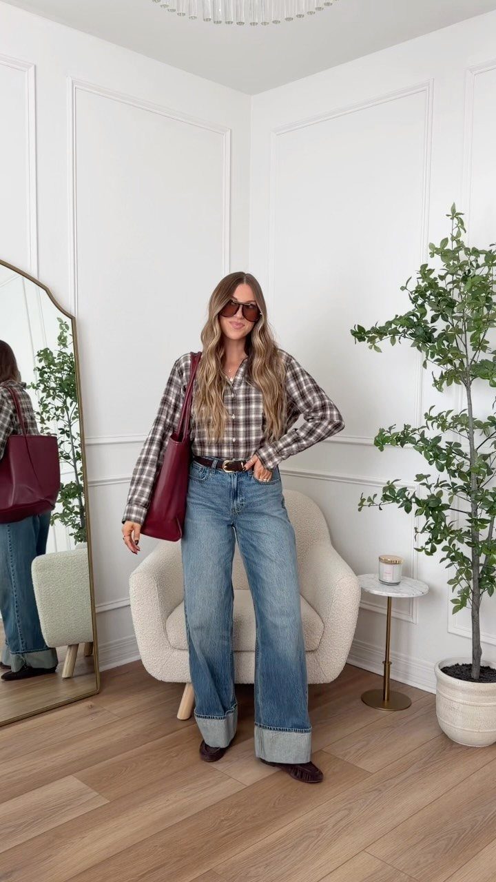 12 Wide Leg Pants Outfit Ideas, From Casual to Polished 8 Woman wearing cuffed wide-leg blue jeans and a plaid shirt in a bright room.