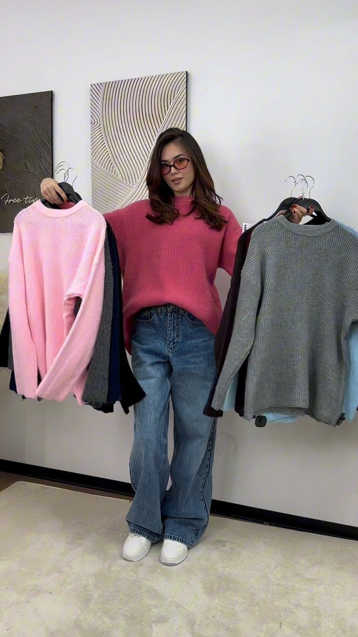 12 Wide Leg Pants Outfit Ideas, From Casual to Polished 7 Woman wearing a pink slouchy sweater and wide-leg blue jeans with white sneakers.