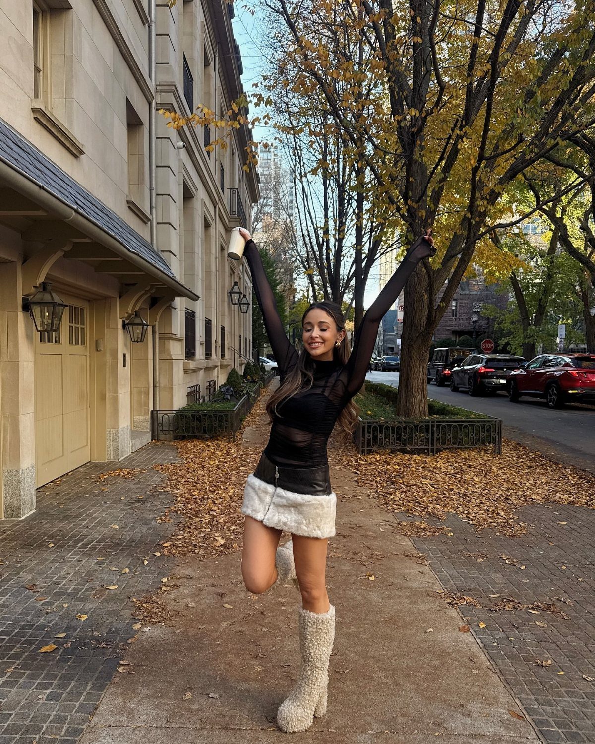 Woman in a black sheer top, white fluffy skirt, and faux-fur boots posing outdoors.
