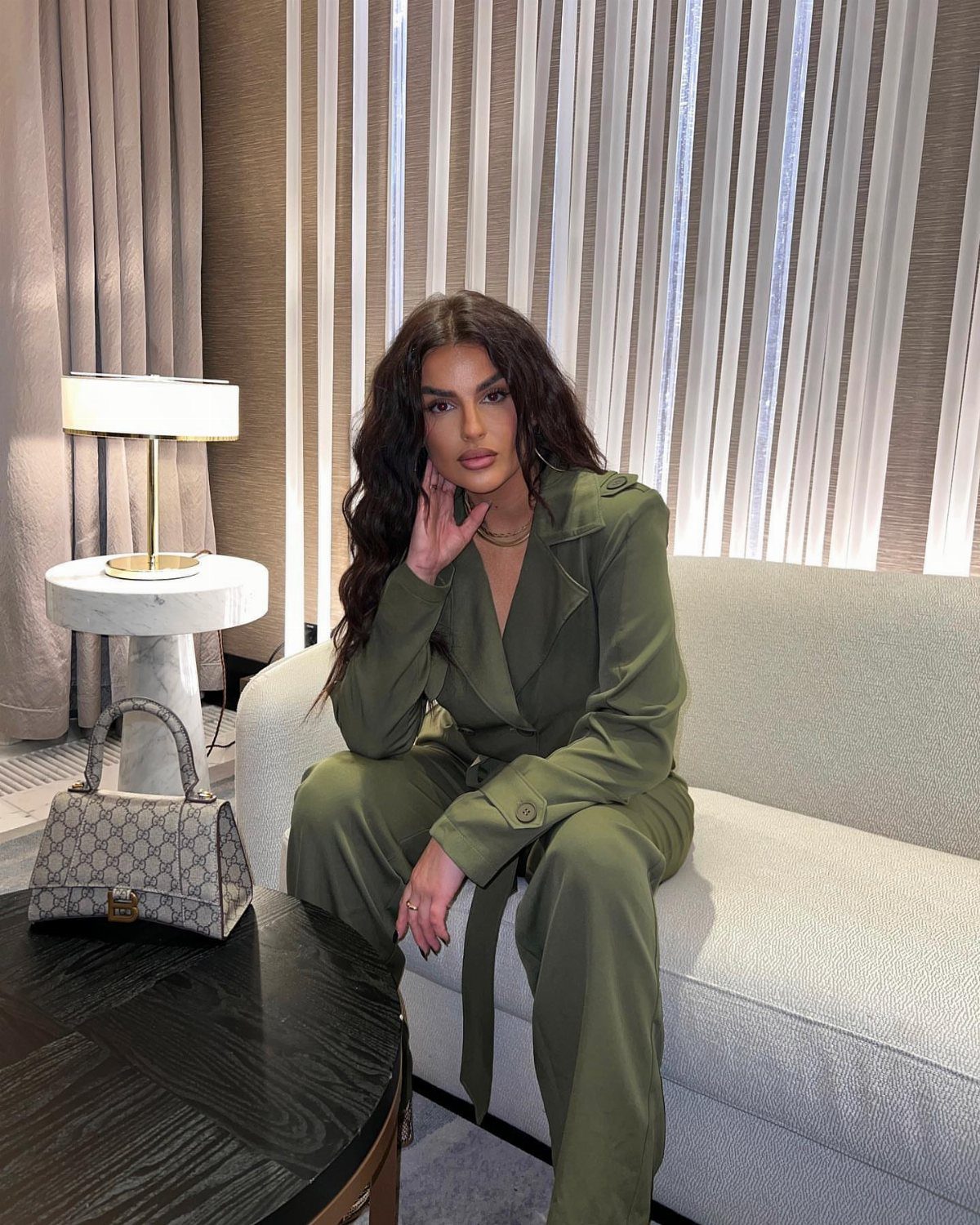 Women Travel Outfit: 8 Looks for Airport to City 4 Woman in an olive green jumpsuit sitting on a light grey sofa in a room.