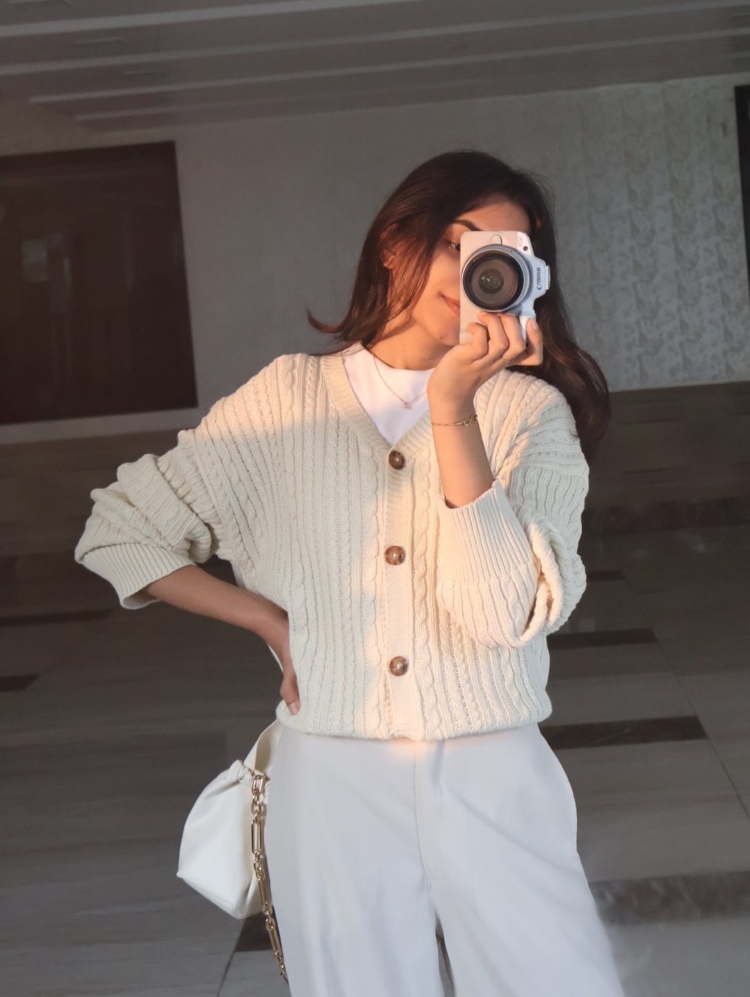 Women's Business Casual: 10 Outfit Ideas for the Office 7 Woman in a cream ribbed cardigan and white trousers taking a mirror selfie with a camera.