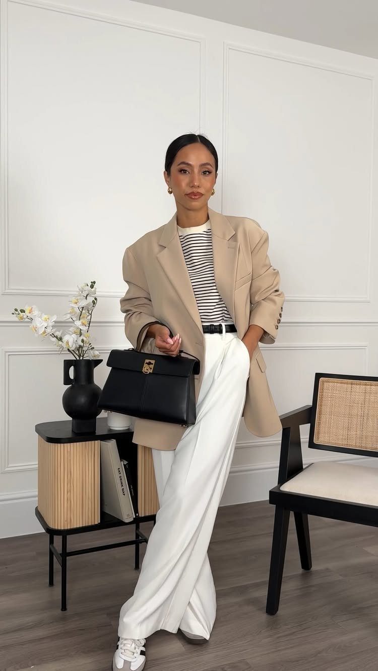 Women's Business Casual: 10 Outfit Ideas for the Office 8 Woman in a tan blazer, striped shirt, and white trousers posing with a black handbag.