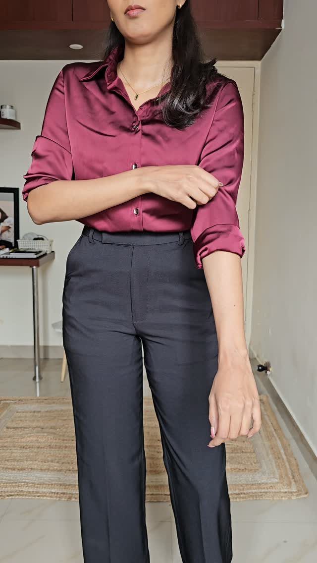 Work Outfits for Women: 7 Smart Office Looks for 2026 3 A woman wearing a maroon satin shirt and dark grey tailored trousers standing in a room.