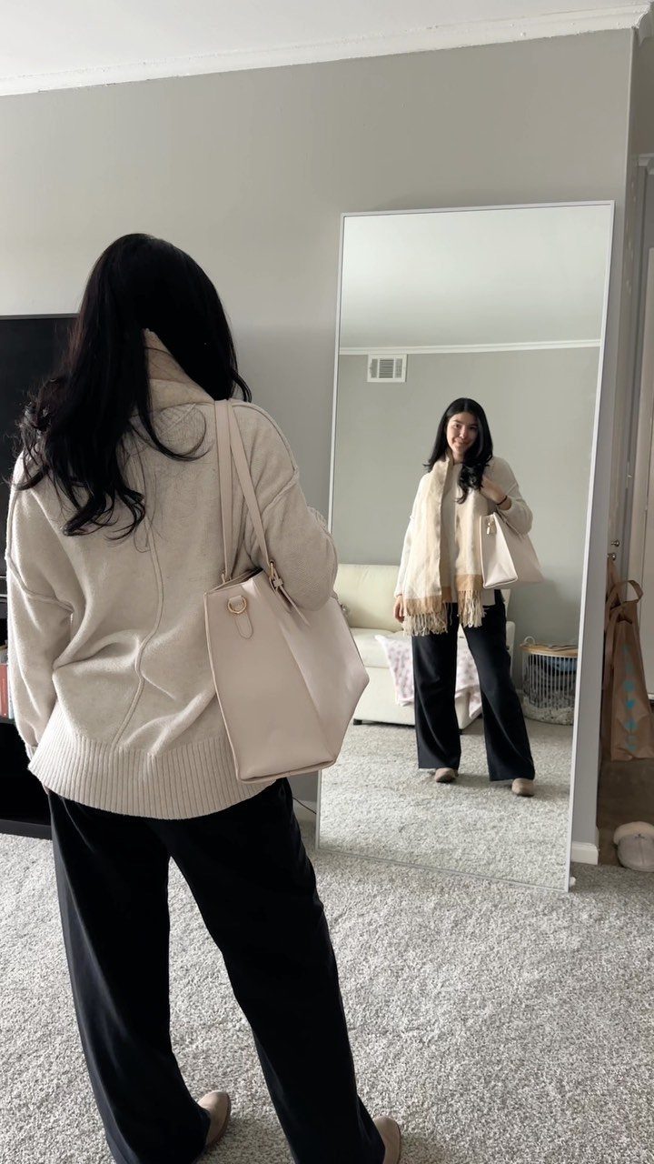 Work Outfits for Women: 7 Smart Office Looks for 2026 6 Woman wearing a cream sweater and black wide-leg pants standing before a mirror.