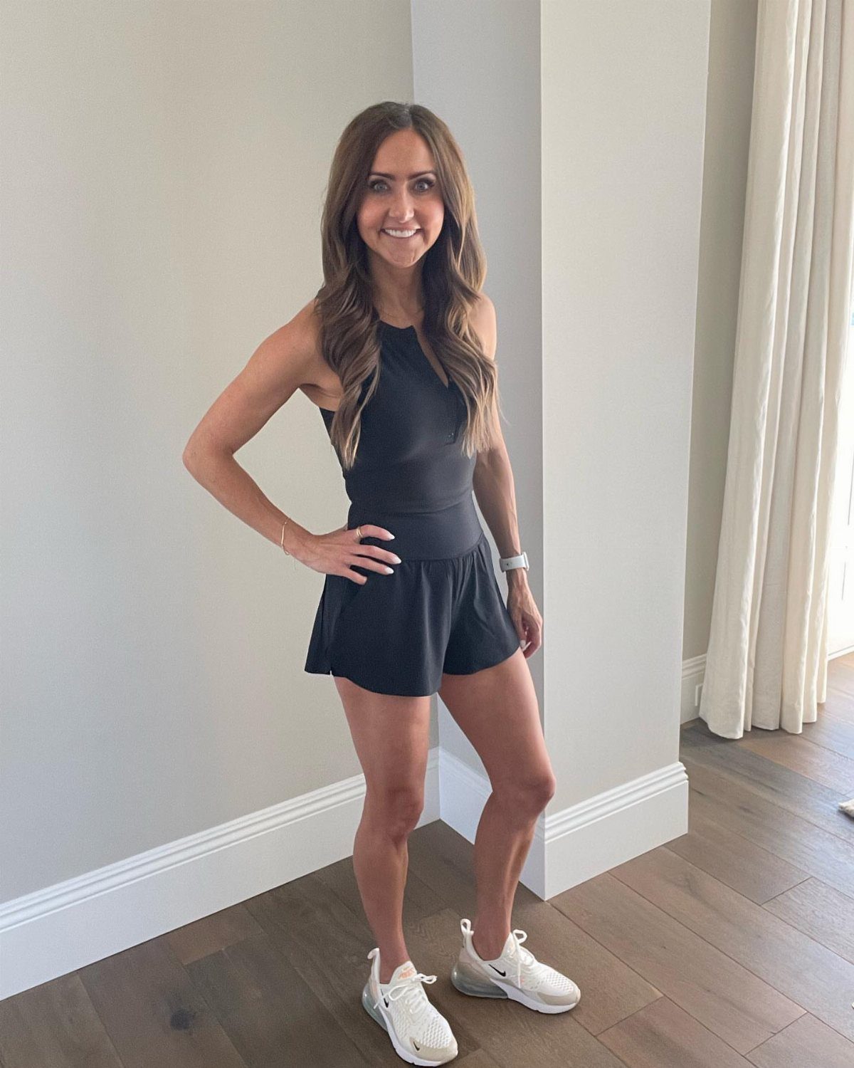 Woman wearing a black athletic tank top and shorts with white sneakers.