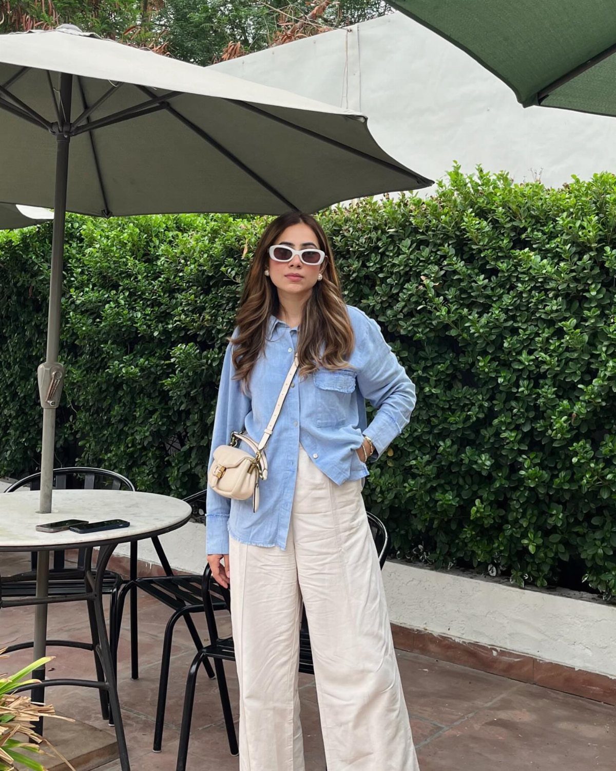 Woman wearing a light blue shirt and cream wide-leg trousers standing outdoors.