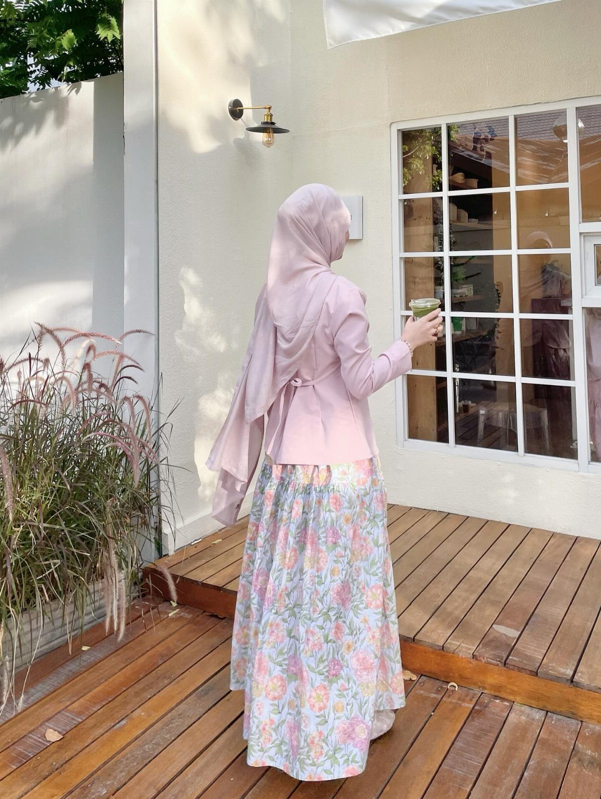 Woman in pink blazer and floral skirt standing on a wooden outdoor deck.