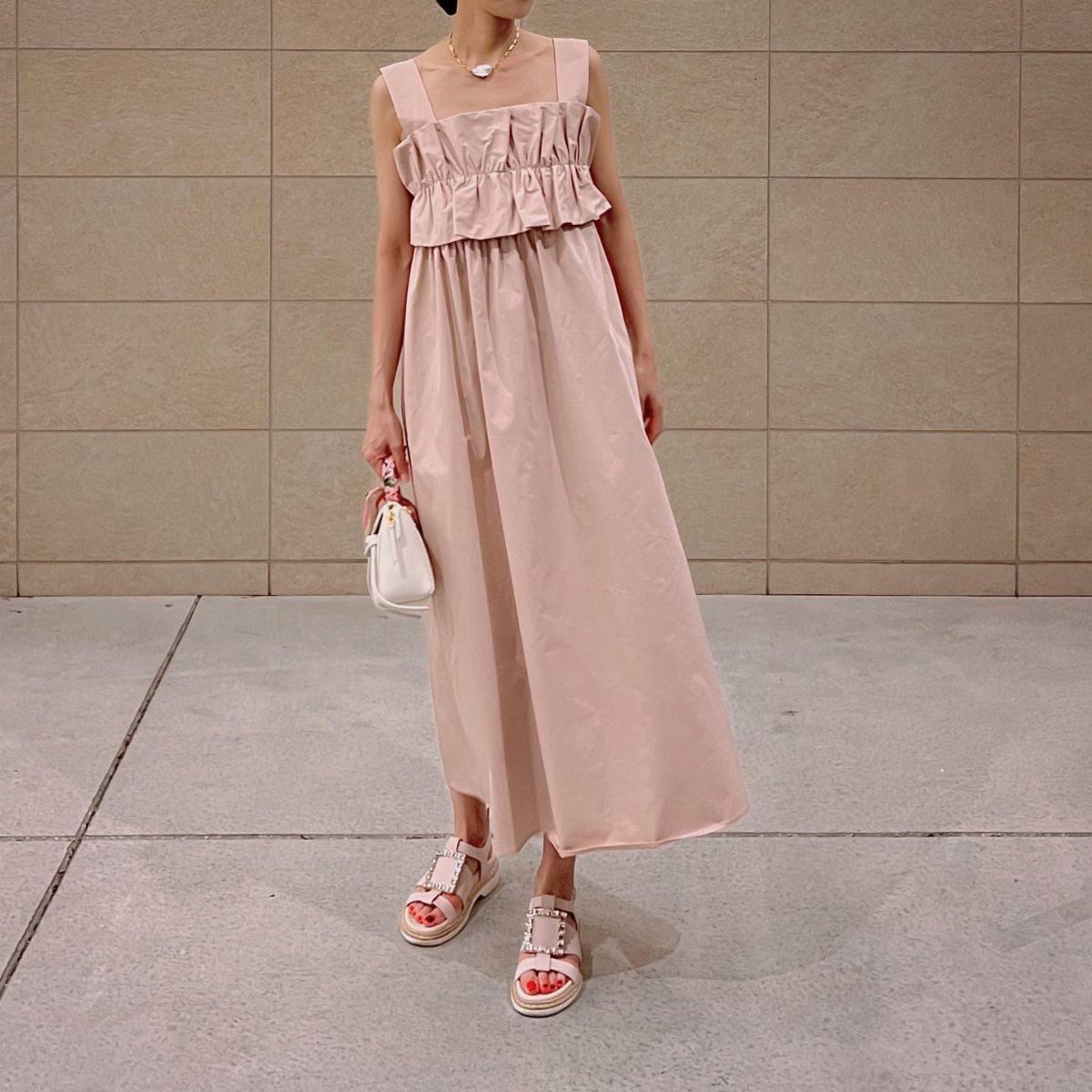 Person in a light pink maxi dress and flat sandals holding a white handbag.
