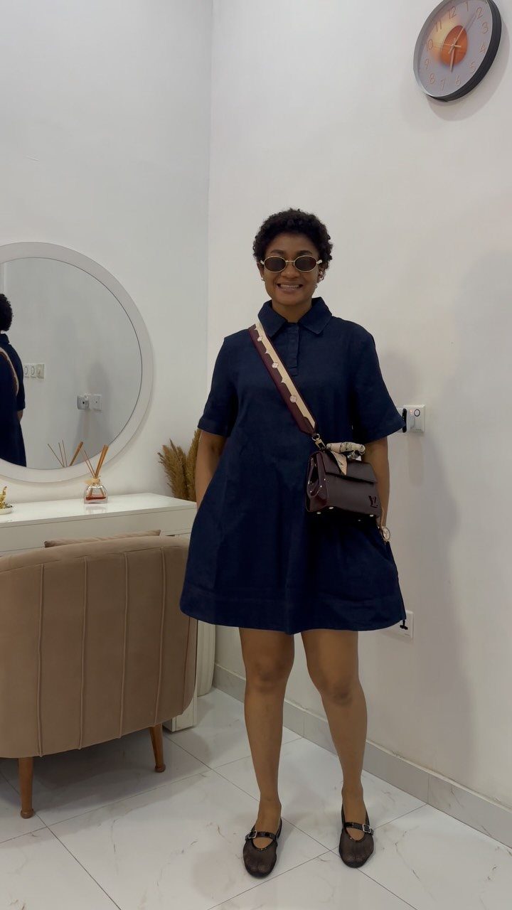 Woman wearing a navy blue shirt dress and sunglasses posing in a room.