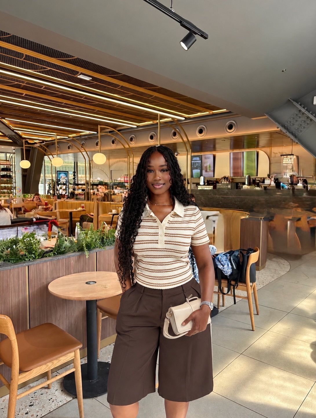 Woman wearing a striped polo shirt and brown chino shorts in a cafe.