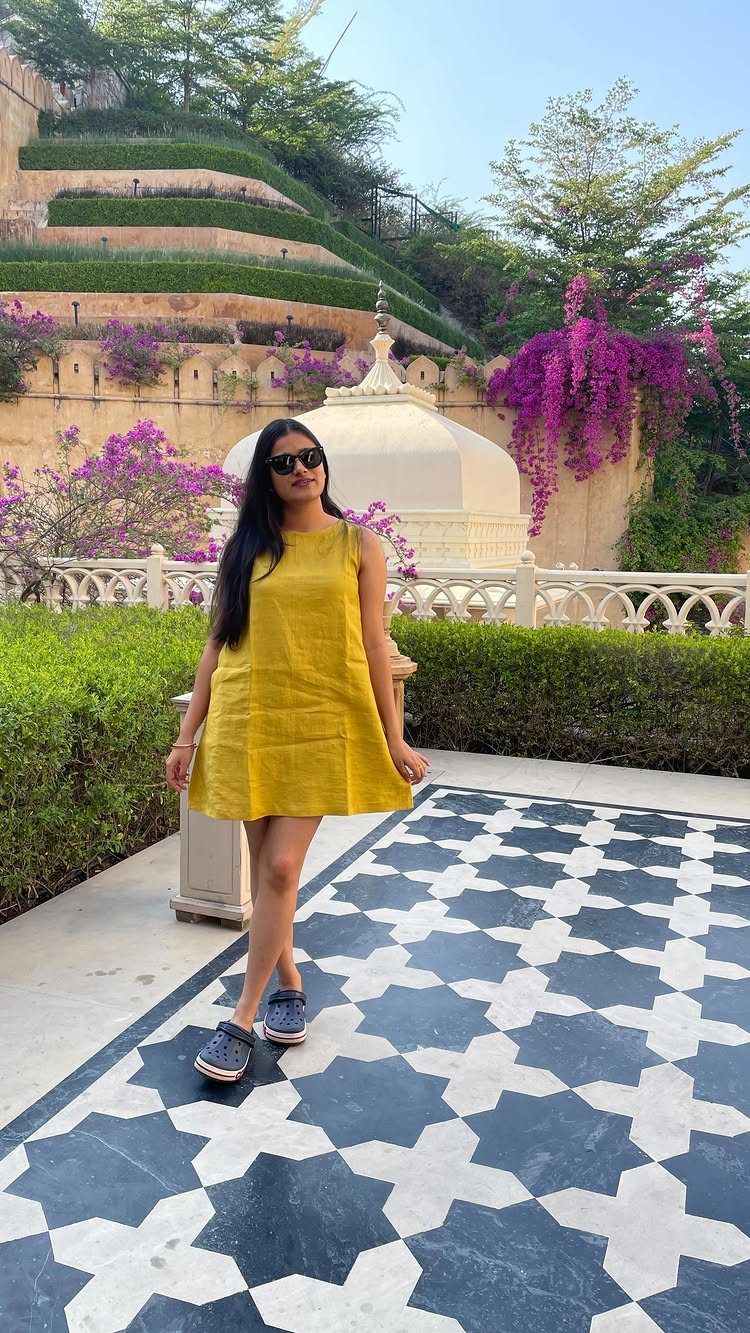 Woman in a sleeveless yellow dress and blue shoes standing on patterned tiles.