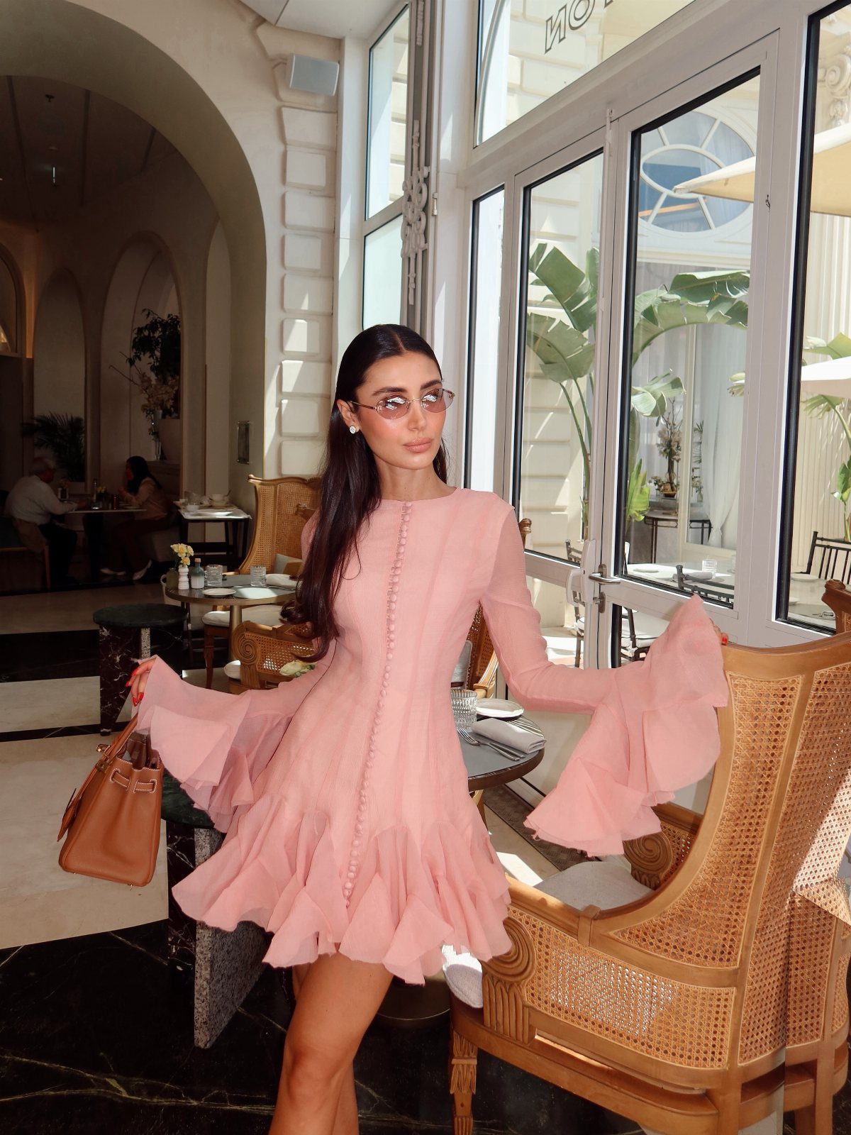 Zara Summer Dresses From Mini to Maxi (21 Characters) 11 Woman in a short pink ruffled dress holding a brown handbag in a bright room.