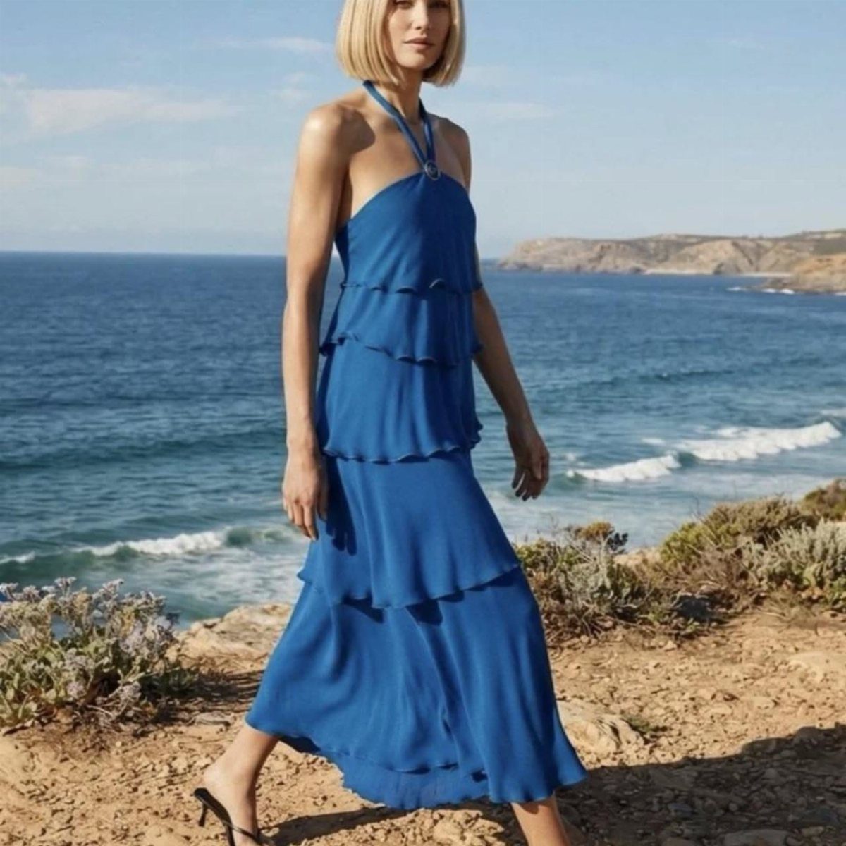 Zara Summer Dresses From Mini to Maxi (21 Characters) 9 Woman in a royal blue tiered halter maxi dress standing by the ocean.
