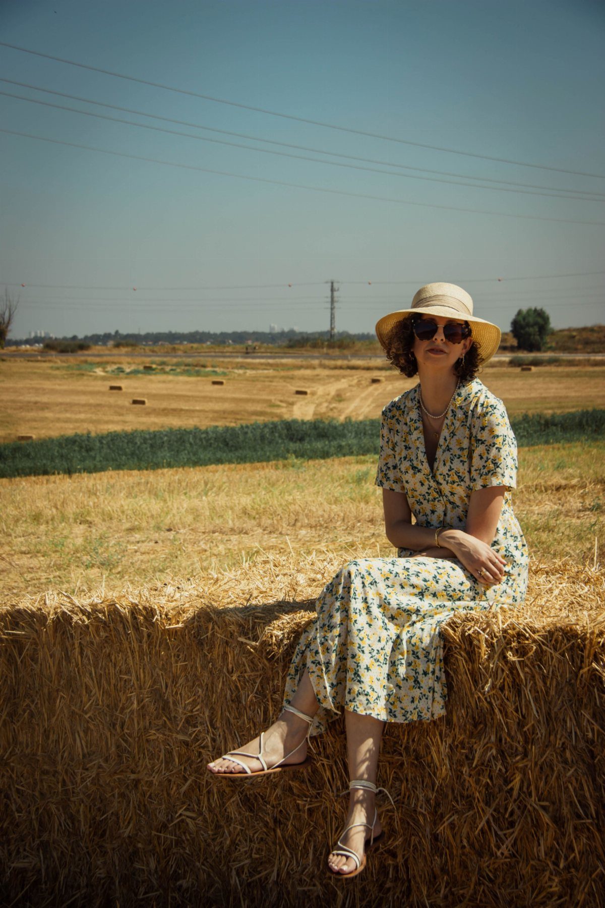 Zara Summer Dresses From Mini to Maxi (21 Characters) 7 Woman in yellow floral midi dress and straw hat sitting on hay bale.